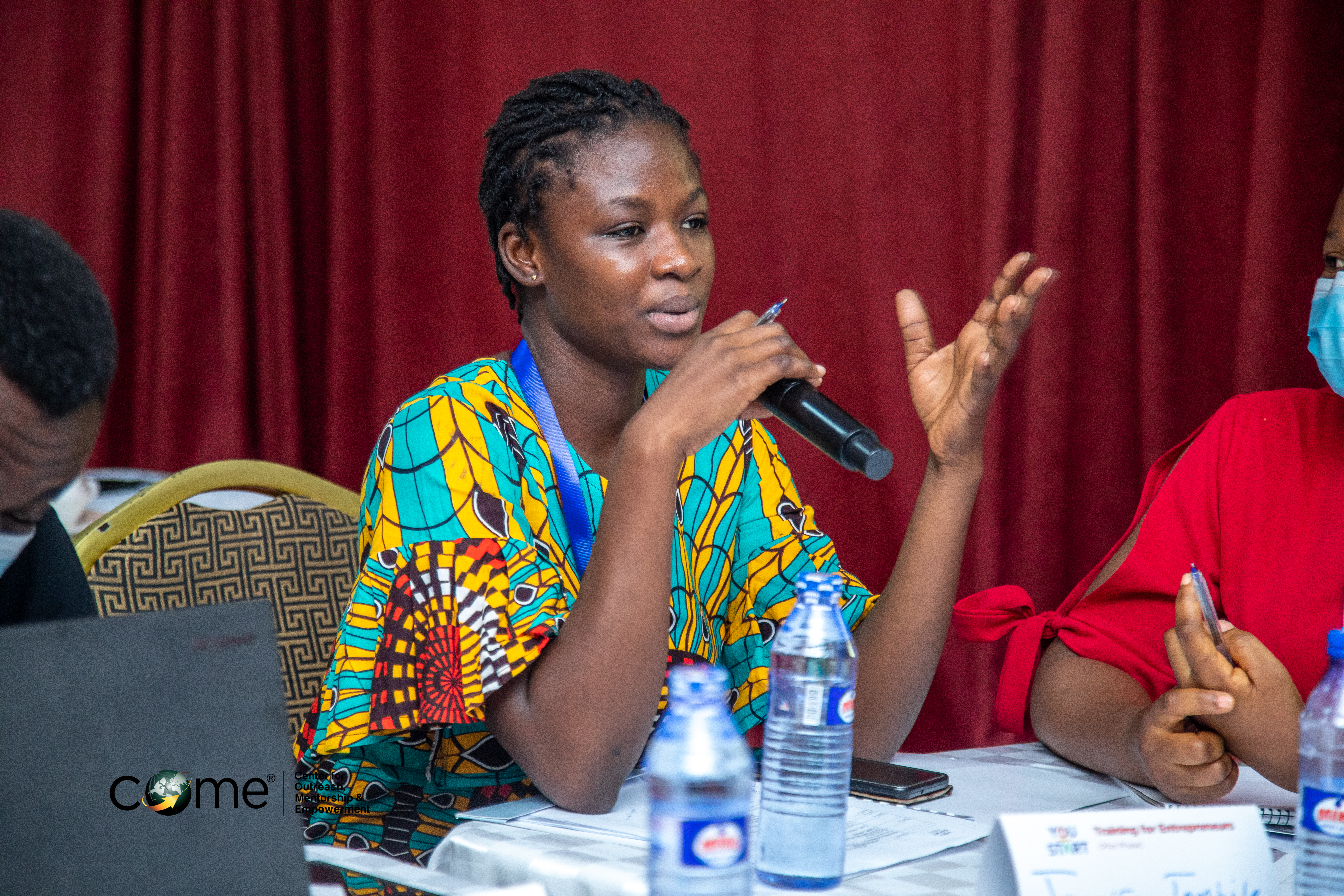 Participant speaking into a microphone at a COME training and entrepreneurship session.